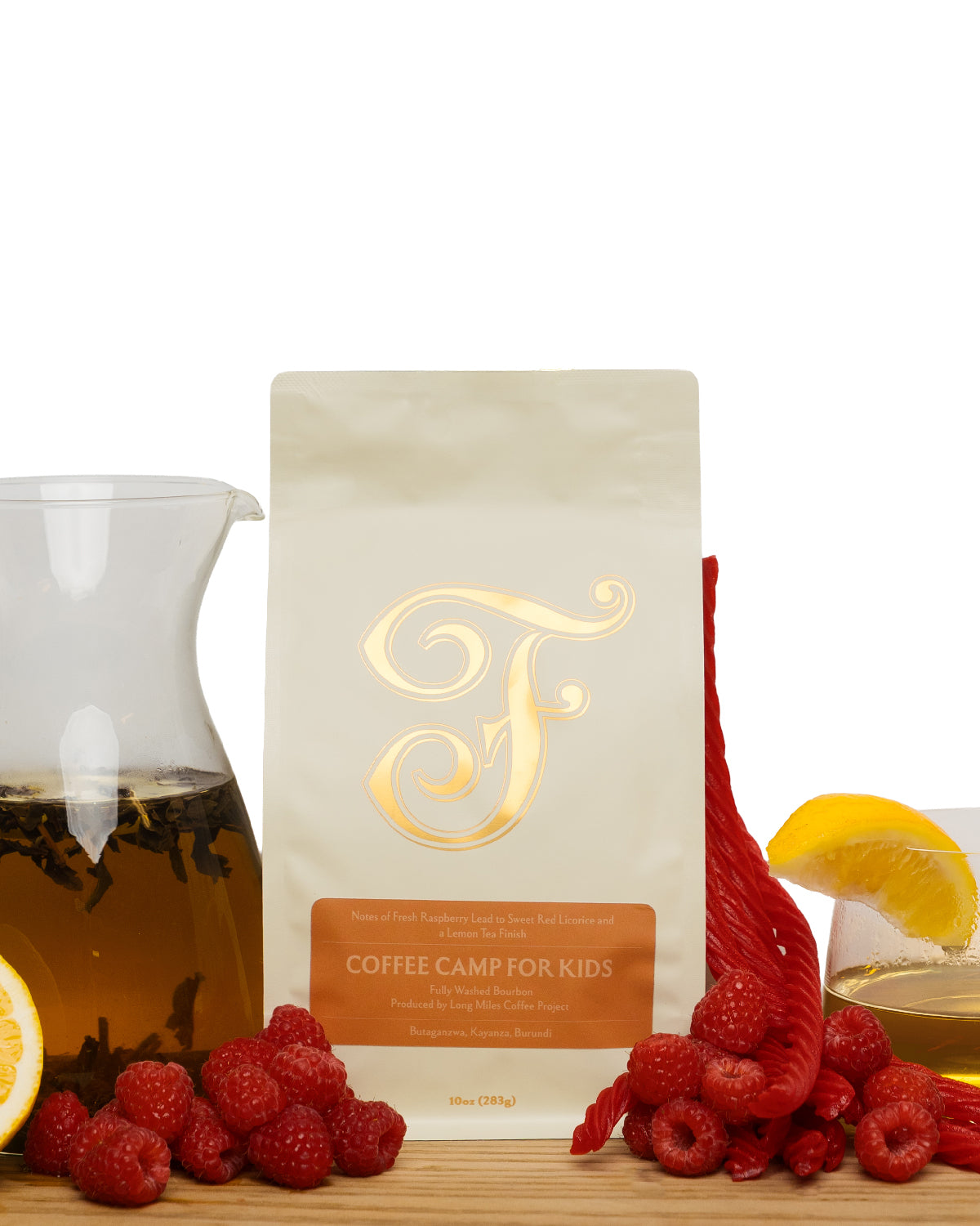 A stand-up pouch of coffee for kids stands on a wooden surface with a glass carafe of brewed coffee, raspberries, and citrus slices around it on a white background.